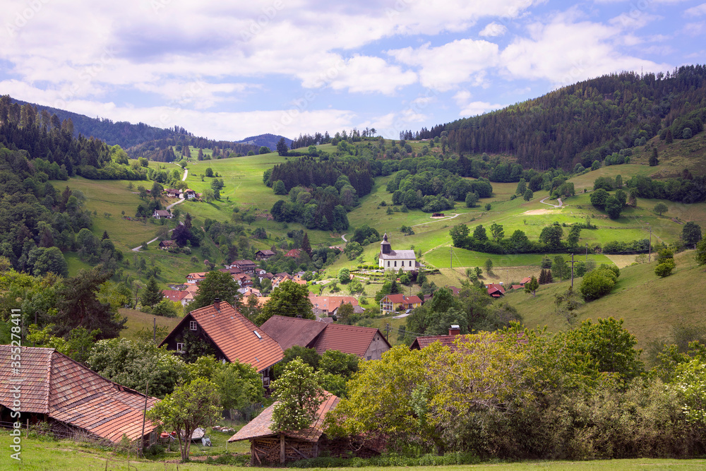 Beautiful landscape with Schwarzwald mountains, village in the valley with church. Hills with green meadows and forest, blue sky. Black Forest panorama, Germany.