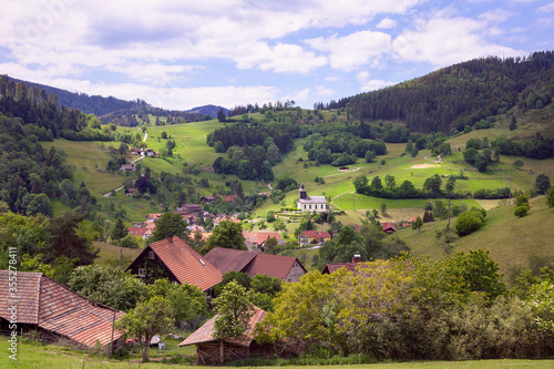 Beautiful landscape with Schwarzwald mountains, village in the valley with church. Hills with green meadows and forest, blue sky. Black Forest panorama, Germany.