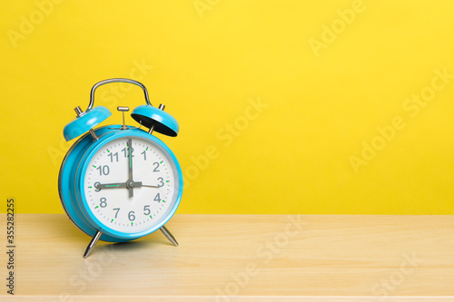 Blue vintage alarm clock at nine o’ clock on a yellow background with space for copy