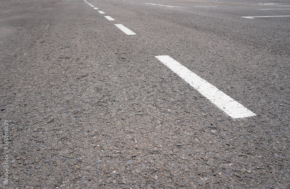 Dark asphalt road with marking lines. Tarmac texture. White disabled sign on a empty parking lot. Black tarmac texture with road marking 