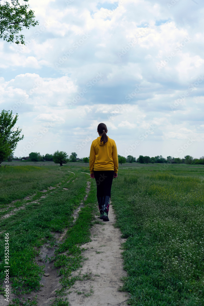 Girl in yellow walking on countryside path at early spring