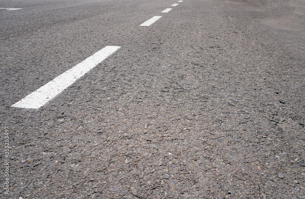 Dark asphalt road with marking lines. Tarmac texture. White disabled sign on a empty parking lot. Black tarmac texture with road marking 