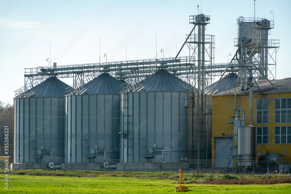 A large modern plant for the storage and processing of grain crops. view of the granary on a sunny day. Large iron barrels of grain. silver silos on agro manufacturing plant for processing and drying A large modern plant for the storage and processing of grain crops. view of the granary on a sunny day. Large iron barrels of grain. silver silos on agro manufacturing plant for processing and drying