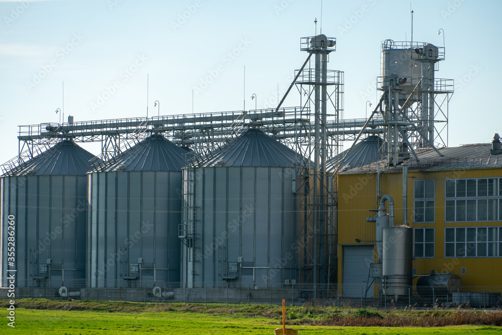 A large modern plant for the storage and processing of grain crops. view of the granary on a sunny day. Large iron barrels of grain. silver silos on agro manufacturing plant for processing and drying A large modern plant for the storage and processing of grain crops. view of the granary on a sunny day. Large iron barrels of grain. silver silos on agro manufacturing plant for processing and drying