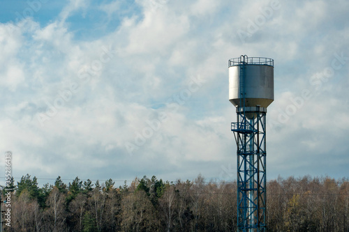 large modern high water tower on sky background with clouds. Forest on the horizon.