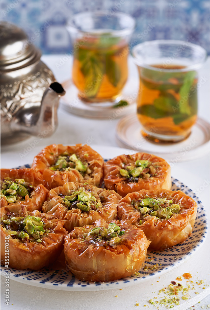 Middle eastern arab sweet pastry baklava with honey, pistachios, mint tea on a light background, selective focus. Ramadan, Eid concept.
