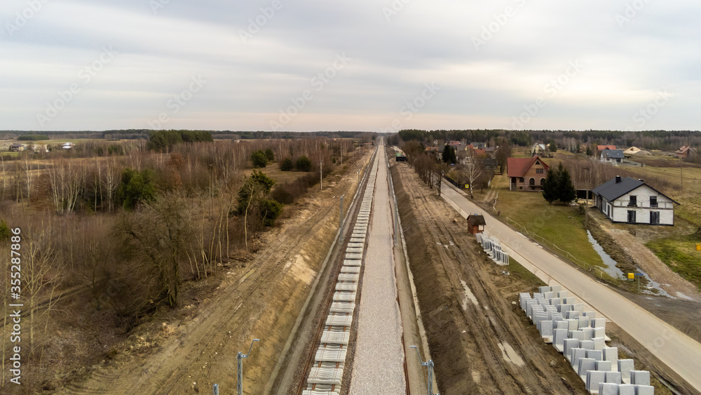 Railway works in small village. Railroad construction and modernisation site. Aerial view on excavator and railway track components. 