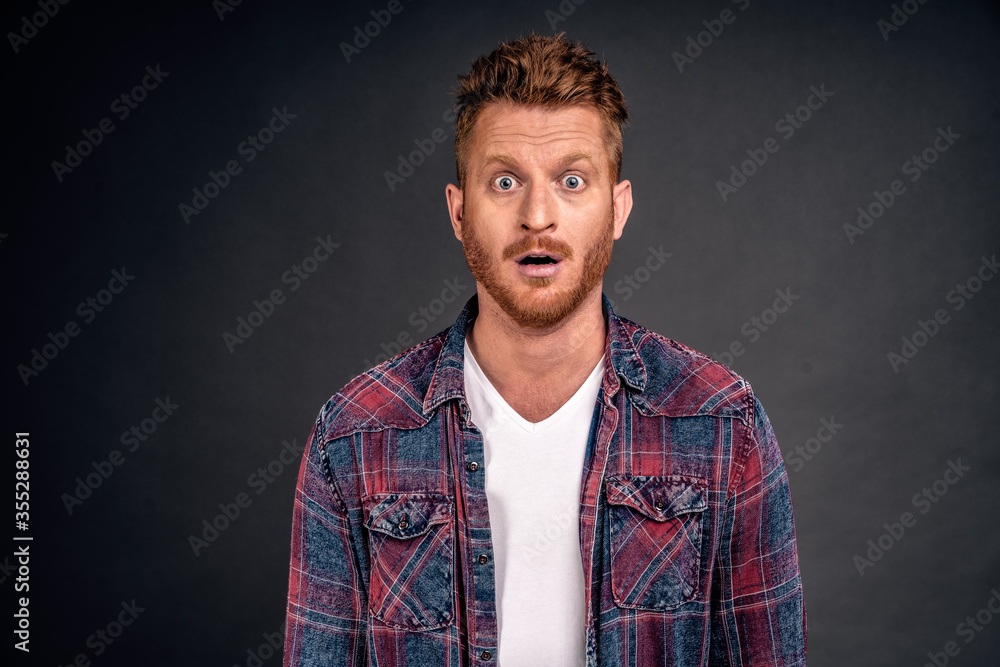Redhead male with bristle dropping jaw as seeing incredible and amazing scenery, posing over gray background in casual shrit, gasping, staring thrilled and astonished at camera over grey wall Redhead male with bristle dropping jaw as seeing incredible and amazing scenery, posing over gray background in casual shrit, gasping, staring thrilled and astonished at camera over grey wall