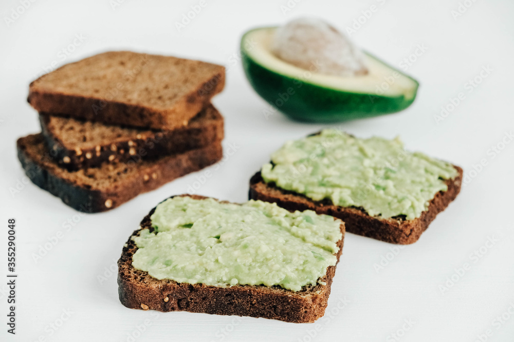 Slices of brown bread with avocado on a white wooden table. Copy, empty space for text