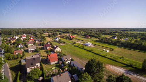 Aerial view on small village in central Poland surrounded by forest. Several houses and empty building plots to be developed. House under construction in center.