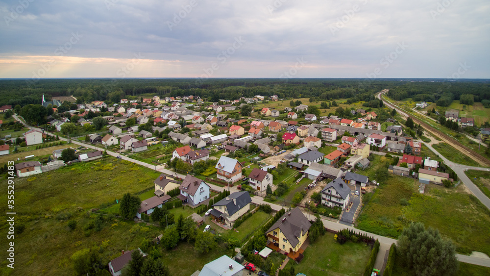 Aerial view on small village located in central Poland. Summer landscape, cloudy afternoon. Green meadows, calm light. Small detached houses,  streets, railroad.
