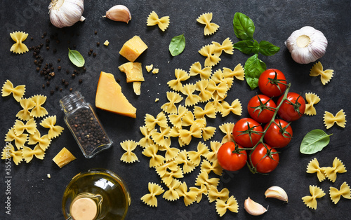 Raw farfolle with tomato and basil on a black background. Top view. Ingredients for making pasta photo