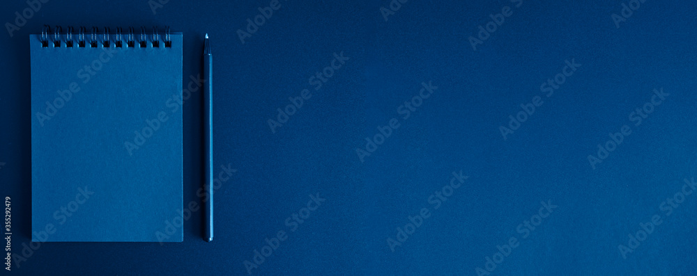 Obraz premium notebook on a spring and a pen on a black background. space for text. banner. toned classic blue color
