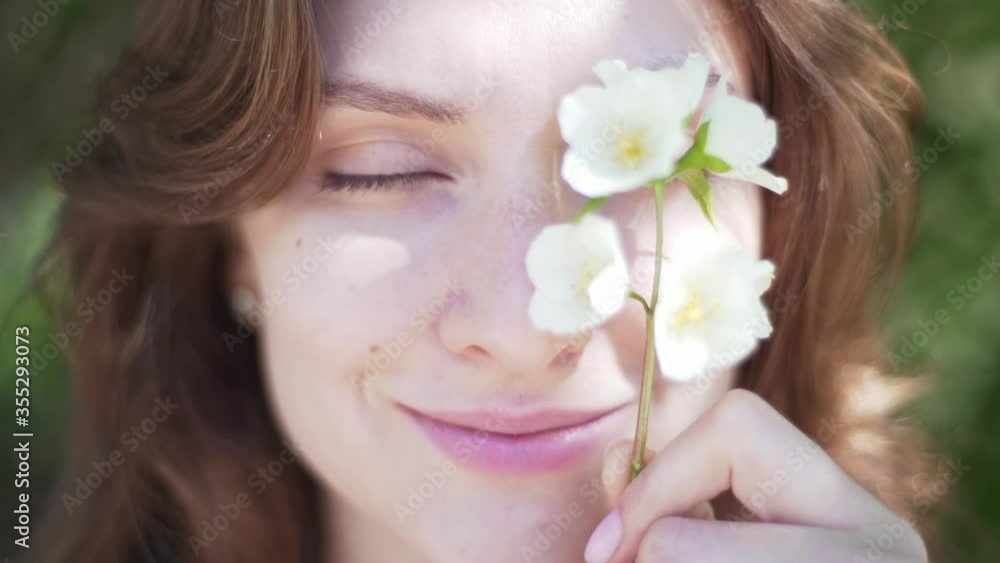 Portrait of a young woman close-up, covering her eye with a branch of jasmine. Beautiful smiling girl with flower in her hand Portrait of a young woman close-up, covering her eye with a branch of jasmine. Beautiful smiling girl with flower in her hand