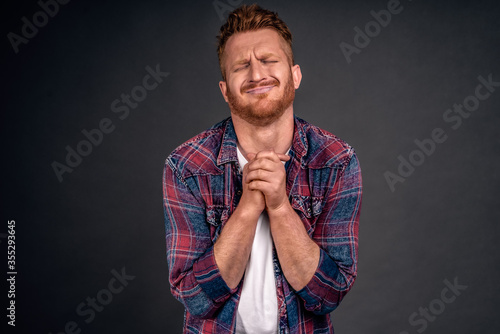 Please honey let me go with guys in pub. Redhead caucasian boyfriend with bristle incheckered shirt, closing eyes frowning, clenching hands together over chest while begging for something passionately