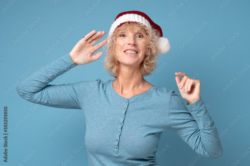 Senior caucasian woman wearing red Santa Claus cap smiling standing on blue wall. Concept of holidays and Christmas Senior caucasian woman wearing red Santa Claus cap smiling standing on blue wall. Concept of holidays and Christmas