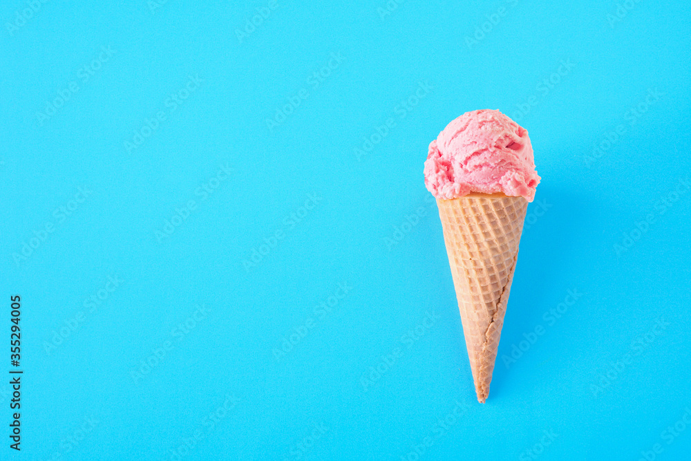 Single cone with pink strawberry ice cream over a blue background. Top view with copy space.