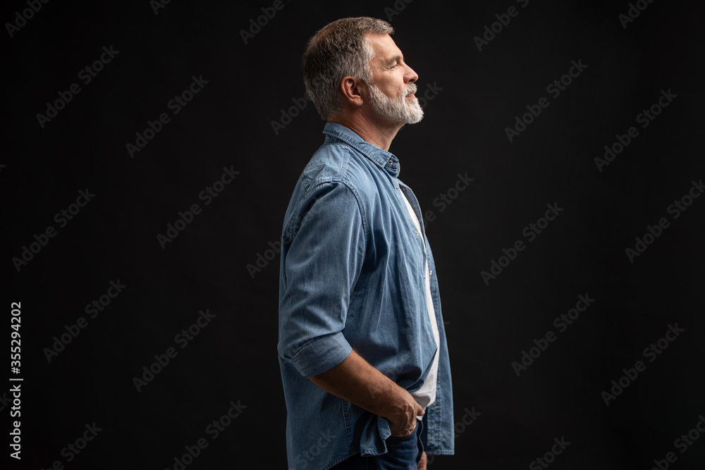 Portrait of smiling mature man standing on black background.