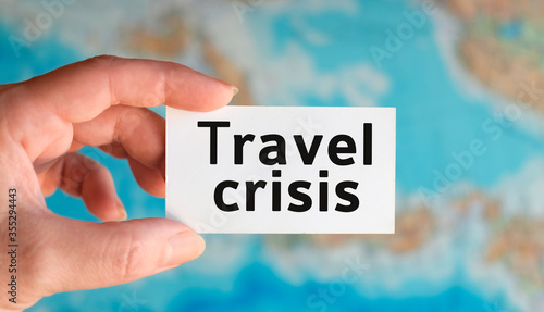 Travel crisis - text on a white sheet in hand against the background of the atlas map