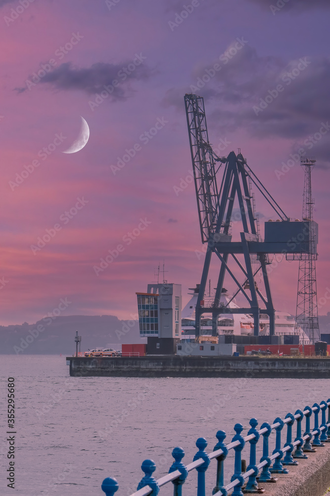 The Large Cranes Ocean Terminal Greenock Early in the Morning with a dramatic sunrise sky and a quarter moon above the giant Greenock cranes