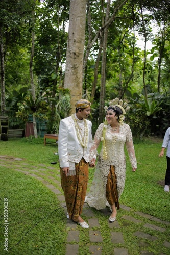 Bride and groom walking in the blossoming spring garden. Javanese traditional bridal concept.