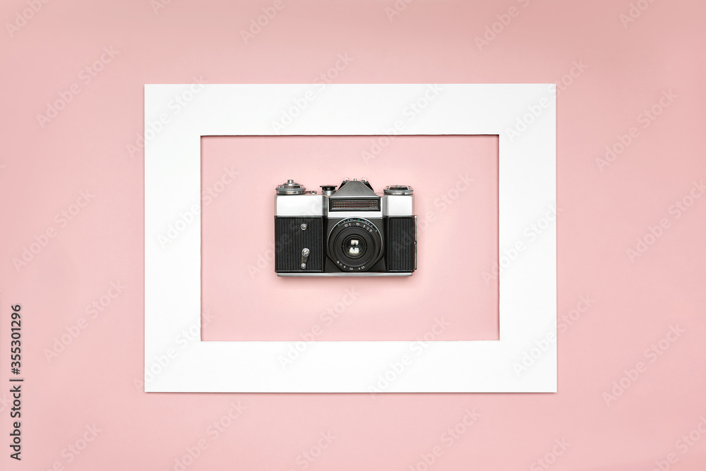 Flat lay old analog camera in the paper white frame on pink background Flat lay old analog camera in the paper white frame on pink background
