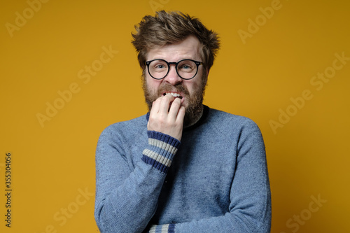 Alarmed hipster with glasses and an old sweater, looks nervous and bites her nails.