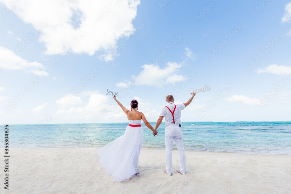 Newlyweds holding hands hugging at white sandy tropical caribbean beach landscape after wedding ceremony of marriage on destination wedding honeymoon travel looking on blue sea in Punta Cana Dominican Newlyweds holding hands hugging at white sandy tropical caribbean beach landscape after wedding ceremony of marriage on destination wedding honeymoon travel looking on blue sea in Punta Cana Dominican
