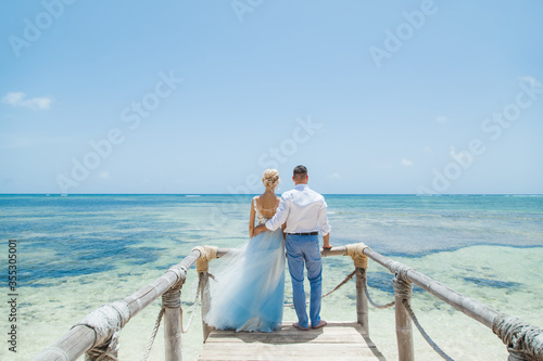 Newlyweds holding hands hugging at white sandy tropical caribbean beach landscape after wedding ceremony of marriage on destination wedding honeymoon travel looking on blue sea in Punta Cana Dominican