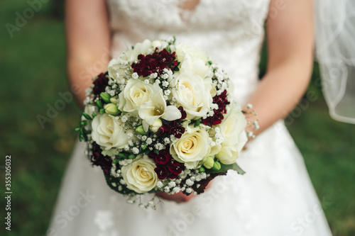 Close up wedding bouquet, white and red flowers. Bride holding flowers in her hands.Outdoor background. Wedding day concept.