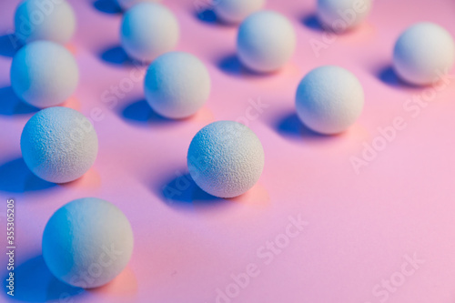 Colored light shines on white balls on a pink background.