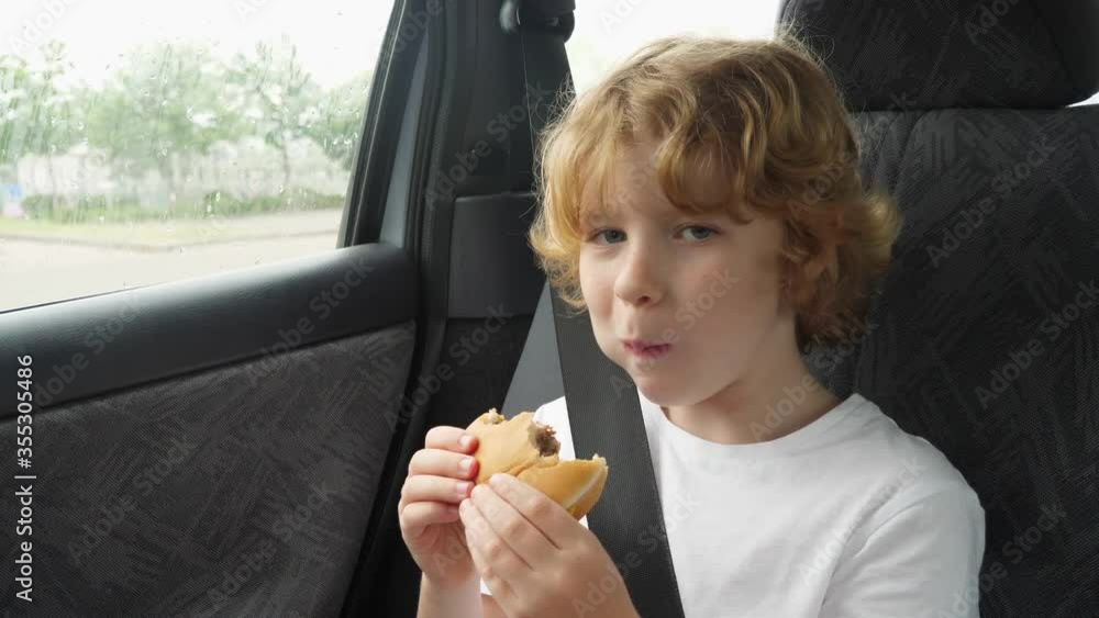 Blonde hungry boy eating a delicious cheeseburger in the car. Blonde hungry boy eating a delicious cheeseburger in the car.
