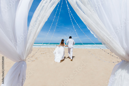 Fotografia Newlyweds holding hands hugging at white sandy tropical caribbean beach landscap