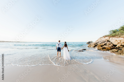 Photographie Newlyweds holding hands hugging at white sandy tropical caribbean beach landscap