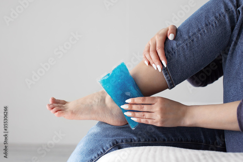Fotografie Close up woman feet and legs, and hands holding ice gel pack as cold compress on