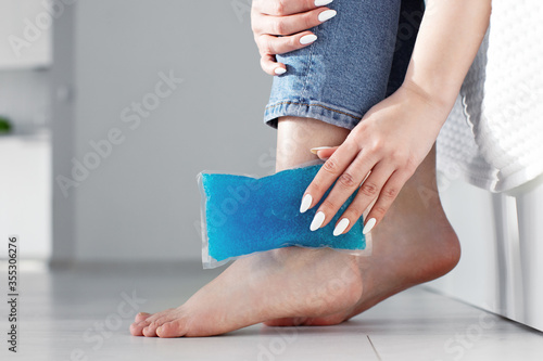 Fényképezés Close up woman feet and legs, and hands holding ice gel pack as cold compress on