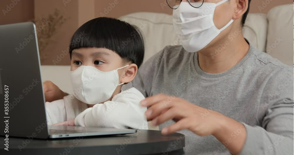 Little boy and father using laptop at home. Boy wearing protective mask with father. He spending time during COVID-19 quarantine. Little boy and father using laptop at home. Boy wearing protective mask with father. He spending time during COVID-19 quarantine.