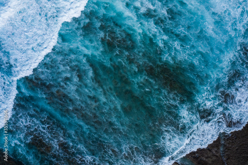 Aerial view directly taken above of some tidal waves coming from the ocean and splashing along the coastline in Indonesia.