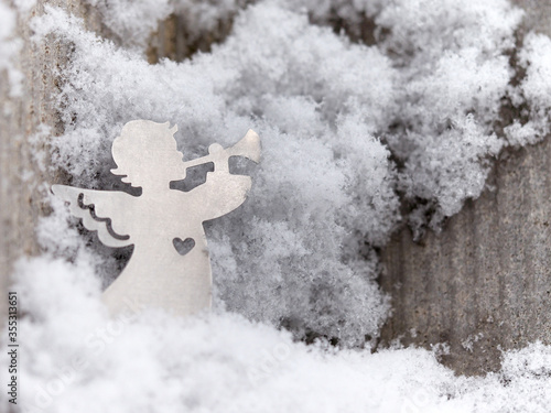 Little flat figure, silhouette of young silver angel with trumpet among the snow flakes on a grey matt background