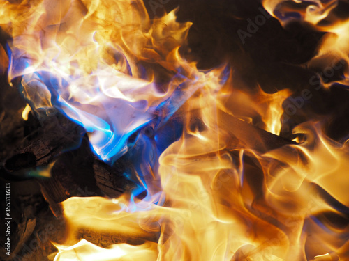 Bizarre colorful flames dancing on the coals of the evening fire; close-up
