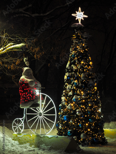 Santa Claus on vintage bicycle near Christmas tree with star on top of it