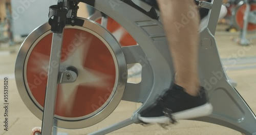 Side view of male feet in sneakers pedaling cycling equipment in sports club. Unrecognizable Caucasian sportsman training on exercise bike in gym. Lifestyle, sport, fitness. Cinema 4k ProRes HQ.