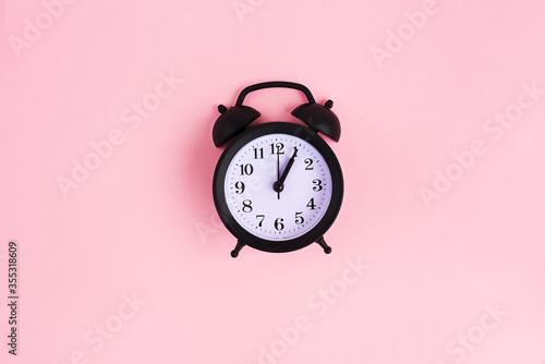 View from above on black alarm clock on pink background. 1 p.m. Time is now