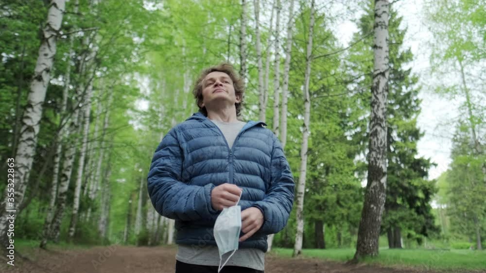 Breathing without mask. Young man stands in the park, takes off the protective mask and starts breathing fresh air deeply Breathing without mask. Young man stands in the park, takes off the protective mask and starts breathing fresh air deeply