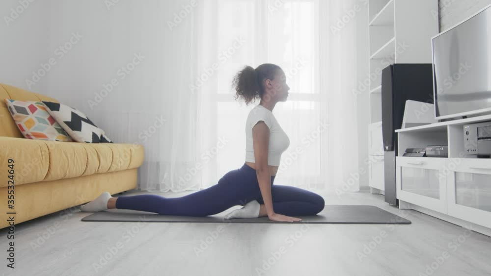 Young sporty african american woman practice yoga at home. Woman does exercises on mat in bright room Young sporty african american woman practice yoga at home. Woman does exercises on mat in bright room
