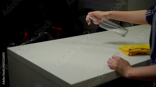 Young woman's hands cleaning a white countertop with a spray bottle. photo