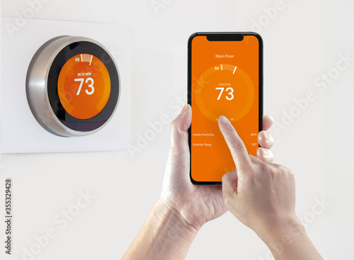 Obraz na plátne A person using a smart phone application warming up the room temperature with a wireless smart thermostat on a white background