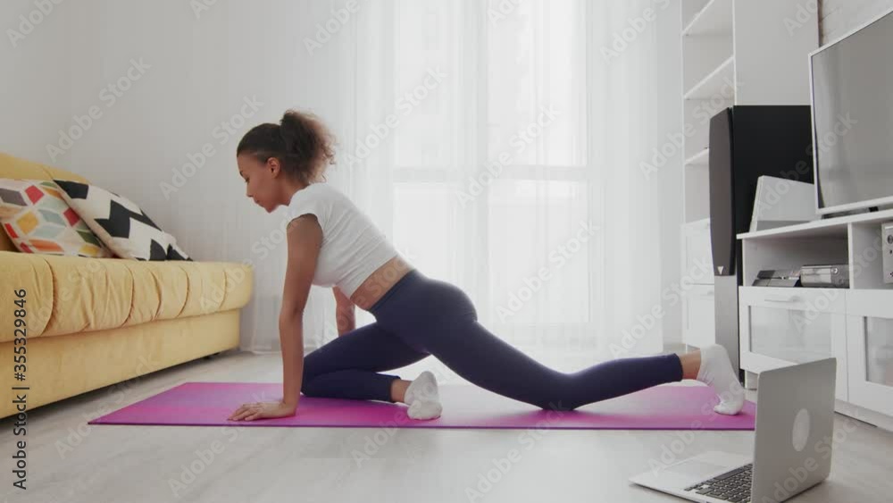 Young sporty african american woman practice yoga on mat with help of her instructor online on laptop at home Young sporty african american woman practice yoga on mat with help of her instructor online on laptop at home