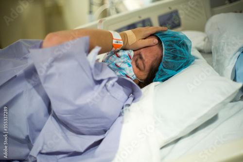 Pregnant woman in labor crying in hospital bed and wearing mask and PPE during Covid-19 pandemic waiting on birth or C-section delivery