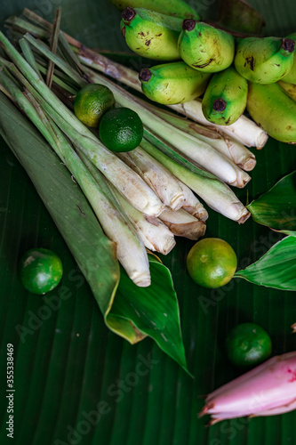 Asian food ingredients such as lemongrass, calamansi, tumeric leaves, torch lily and bananas on a banana leaf background.